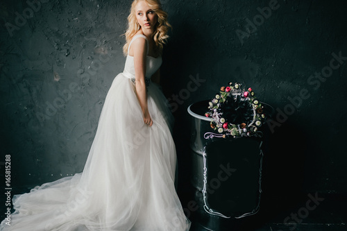 Pinup style portrait of beautiful elegant bride in expensive italian stylish wedding dress showing artisctic emotions on black texture wall background. Cute girl with slender posture and slim body. photo