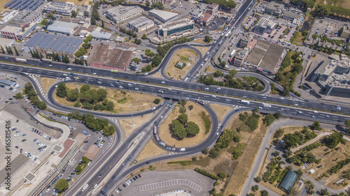 Vista aerea di un uscita autostradale a roma. Le auto corrono veloci lungo l'autostrada mentra alcune si stanno immettendo o ne sta uscendo tramite la corsia di accellerazione o decellerazione. 