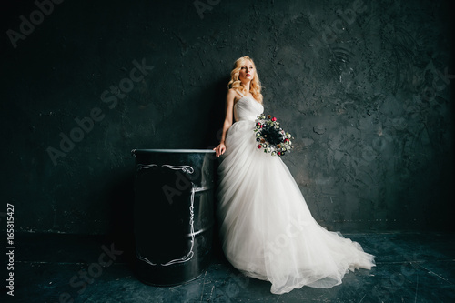 Pinup style portrait of beautiful elegant bride in expensive italian stylish wedding dress showing artisctic emotions on black texture wall background. Cute girl with slender posture and slim body. photo