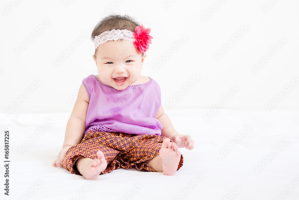 Portrait of a little adorable infant baby girl sitting on the bed and smiling to camera with copyspace Portrait of a little adorable infant baby girl sitting on the bed and smiling to camera with copyspace