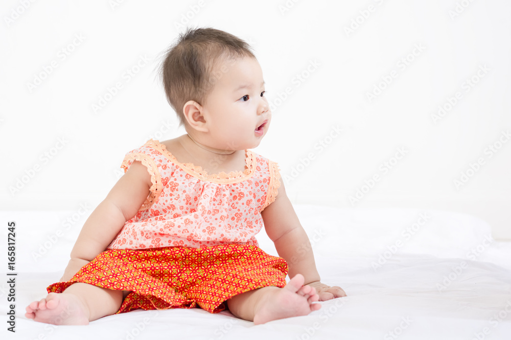 Portrait of a little adorable infant baby girl sitting on the bed and looking to the right side with copyspace Portrait of a little adorable infant baby girl sitting on the bed and looking to the right side with copyspace