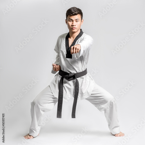 Portrait of an asian professional taekwondo black belt degree (Dan) preparing for fight. Isolated full length on grey background with copy space