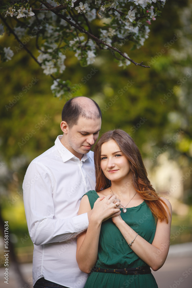 Couple in love: young girl in a long green dress and balding man in the garden. Spring or summer love story Couple in love: young girl in a long green dress and balding man in the garden. Spring or summer love story