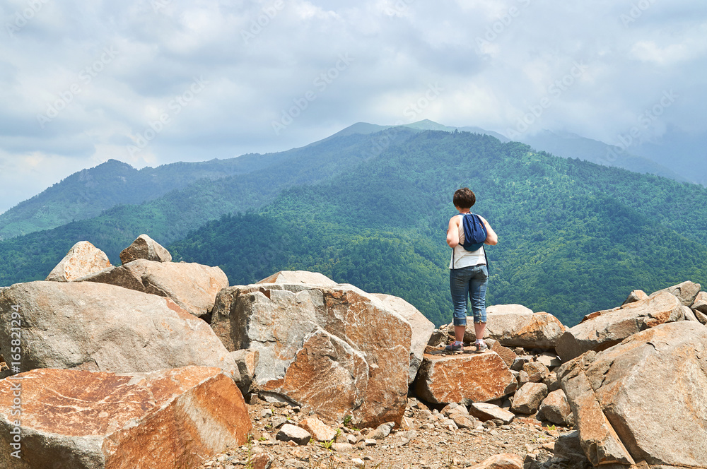 Woman with backpack standing on the rock top and enjoying beautiful view 