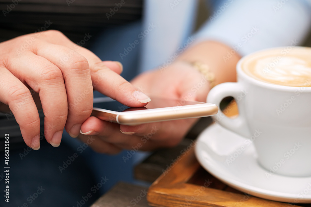 Woman using a mobile phone near a cappuccino cup