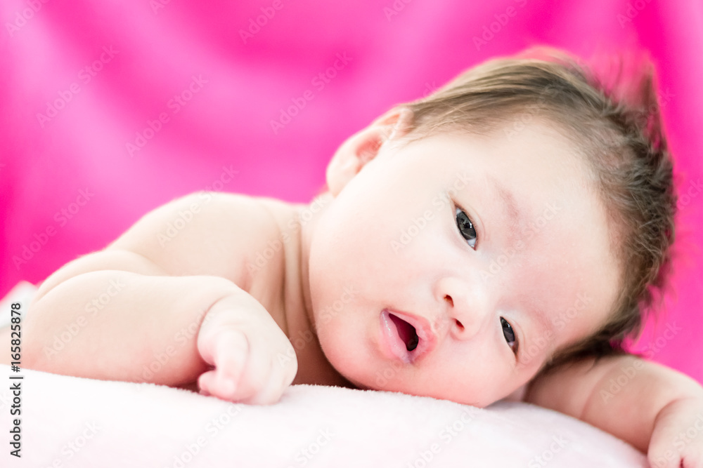 Portrait of a little adorable infant baby girl lying on the tummy on the pillow and looking in camera indoors