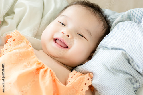Portrait of a little adorable infant baby girl lying on back on blanket and looking in camera indoors