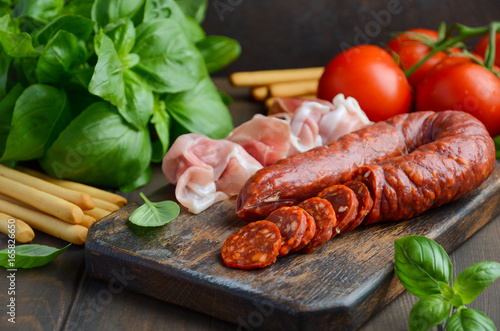 Chorizo sausage. Spanish traditional chorizo sausage and ham with fresh herbs and tomatoes, selective focus.