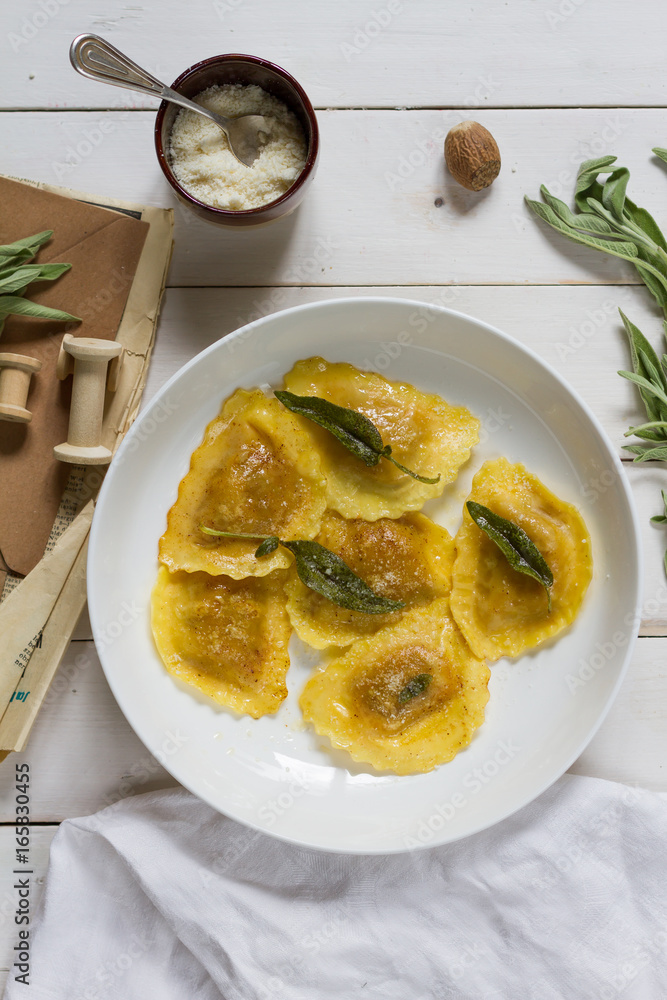 Grilled vegetables ravioli with sage butter. White wooden table, white plate.