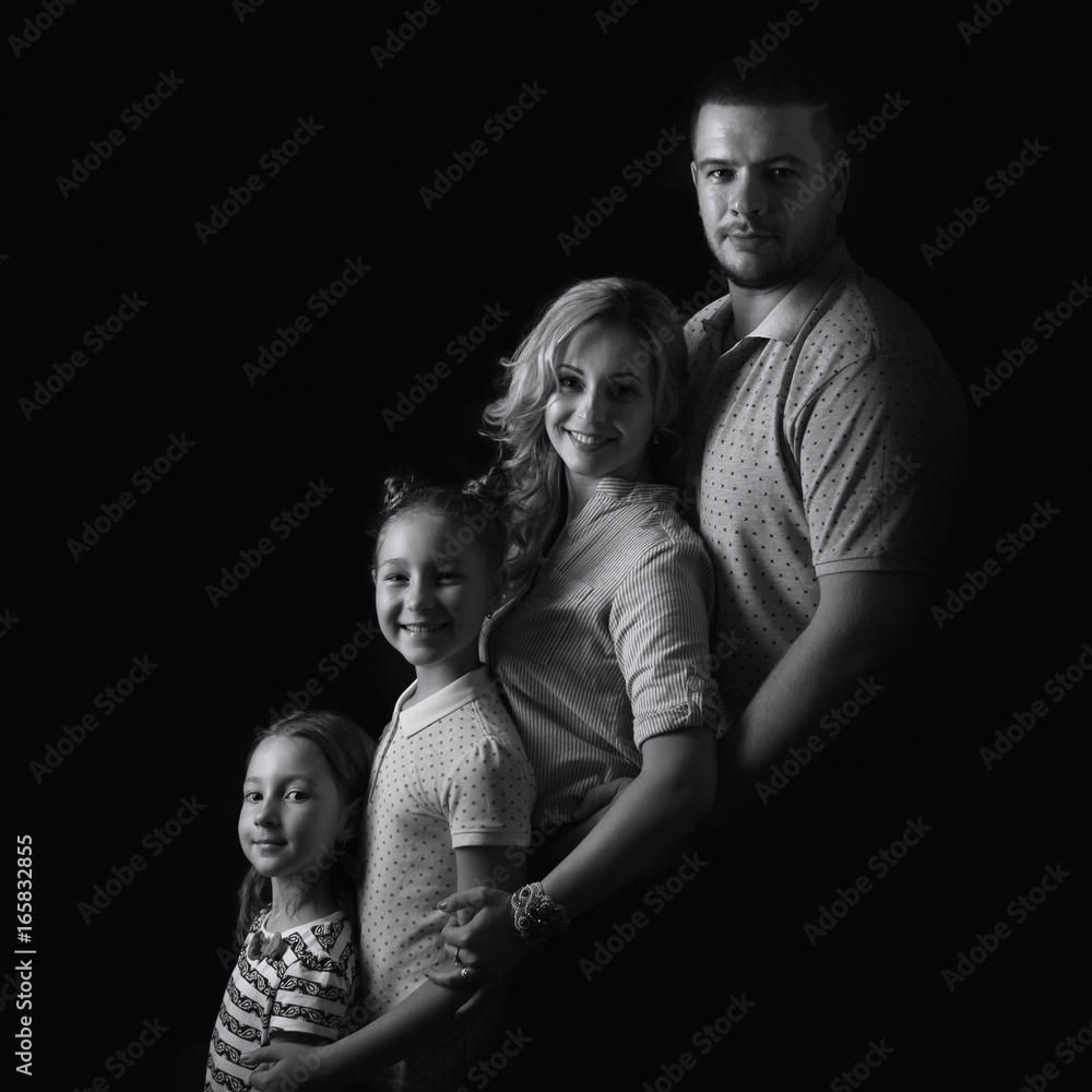 Black and white stufio portrait of young family hugging and posing on