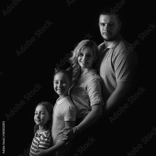Black and white stufio portrait of young family hugging and posing on dark studio background