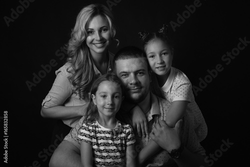 Black and white stufio portrait of young family hugging and posing on dark studio background