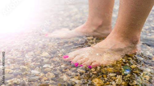 Schöne Füße mit violetten Fußnägeln im flachen Wasser 