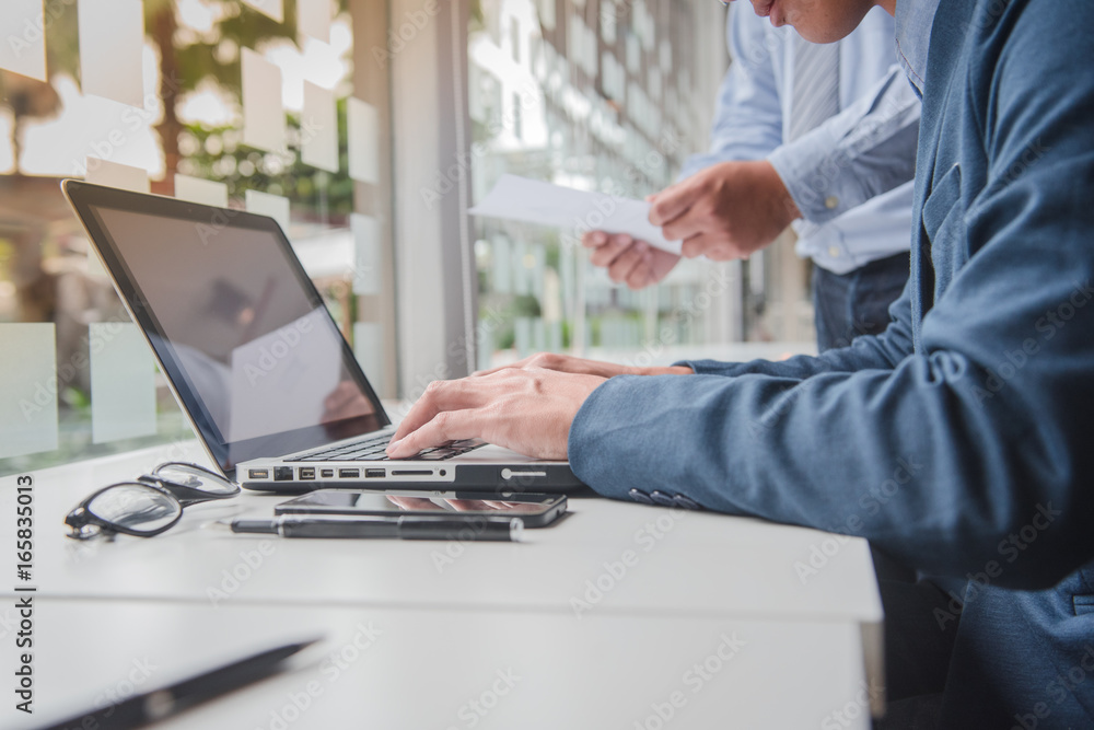 two young businessmen discussing project at meeting with laptop and smart phone on table