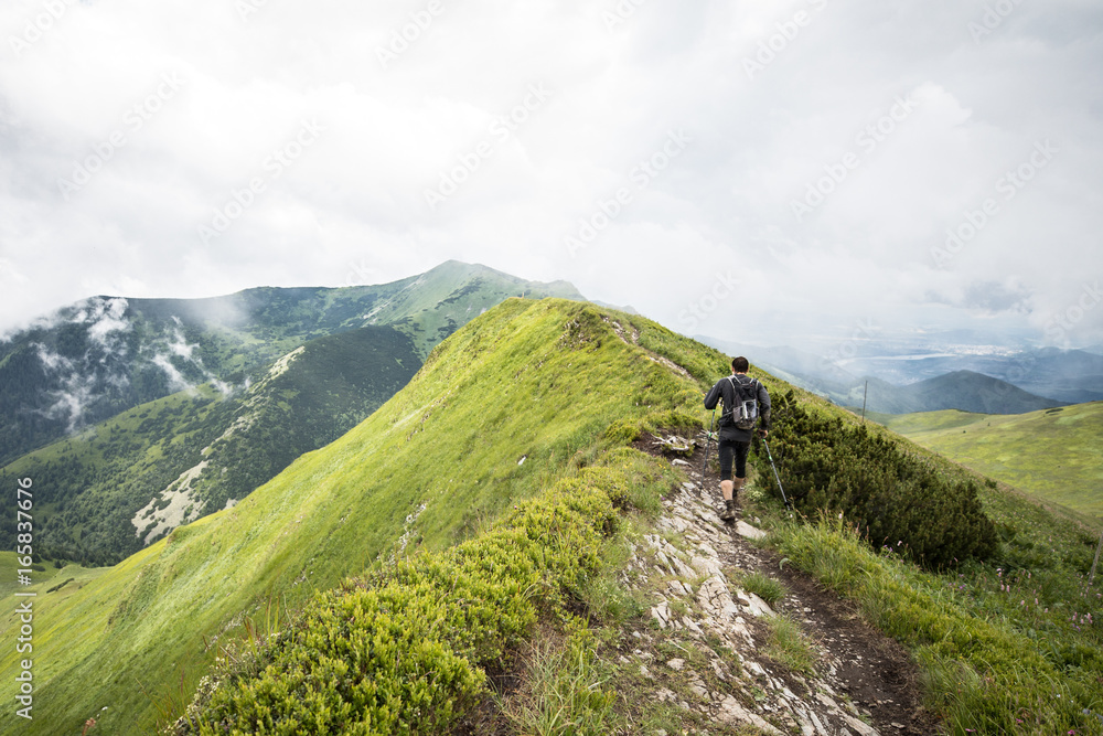 man with hiking poles walking alone on high mountain ridge after summer storm