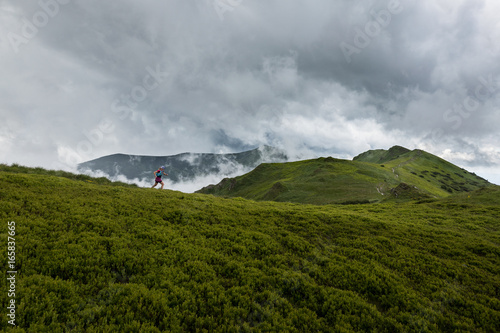 woman running alone outdoors in the summer storm over cloudy mountains trail