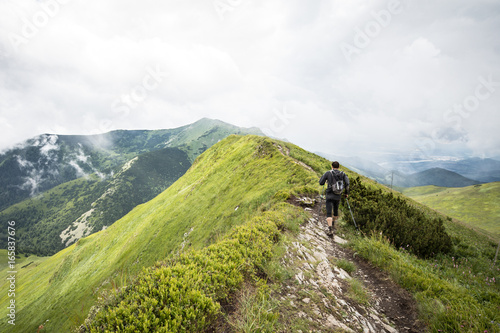 man with hiking poles walking alone on high mountain ridge after summer storm