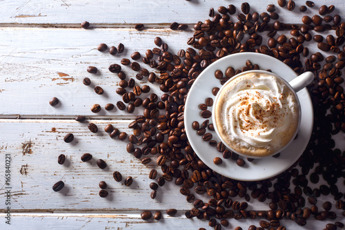 Top view of an irish coffee in a cup with coffee beans around over a white wood table