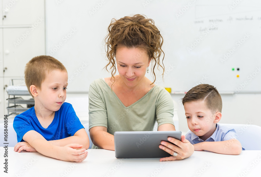 teacher woman using tablet computer with two preschooler boy in a classroom teacher woman using tablet computer with two preschooler boy in a classroom