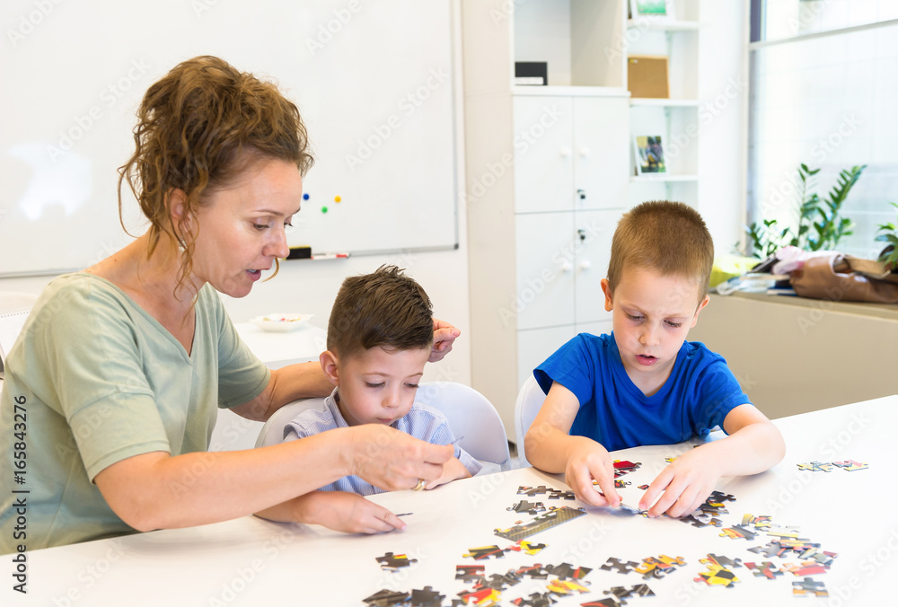 teacher woman and two preschooler boy playing with puzzle game in the classroom teacher woman and two preschooler boy playing with puzzle game in the classroom