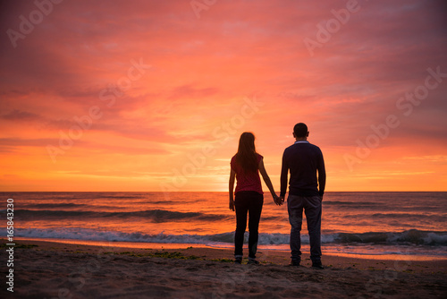 Romantic couple holding hands caring for each other at sunset. Valentines theme. Dramatic sunset. Colorful sky. Sea side romance silhouettes concept
