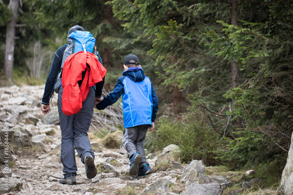 father and son hiking together with backpack up the hill on mountain trail
