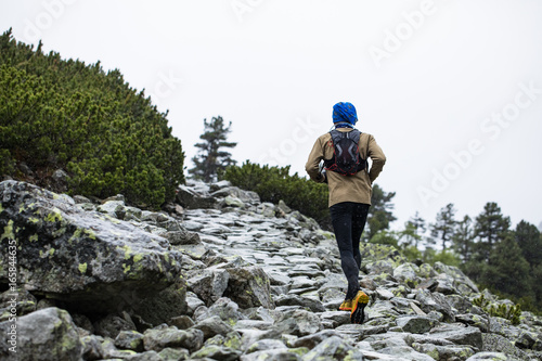 man in warm sportswear running up the hill on cold weather condition with fog and rain