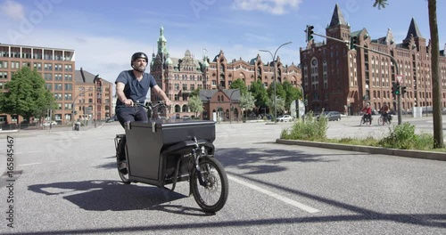 Handsome cargo bike courier is cycling on a street