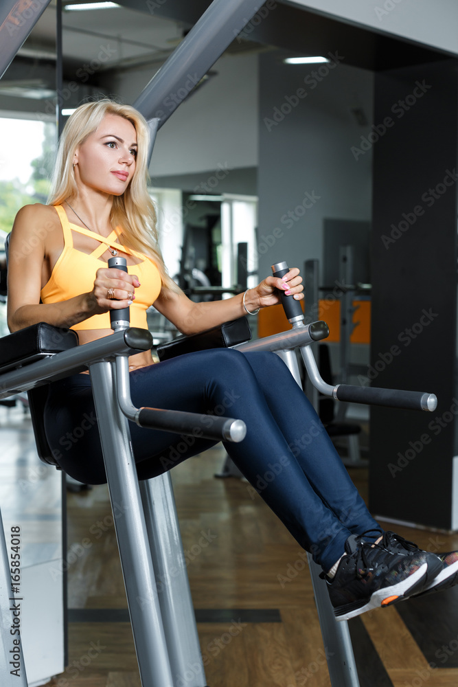 Fototapeta premium Athletic blonde woman using press machine in gym