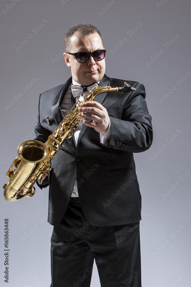 Fototapeta premium Caucasian Saxophone Player in Sunglasses Posing with Saxophone in Studio Environment.
