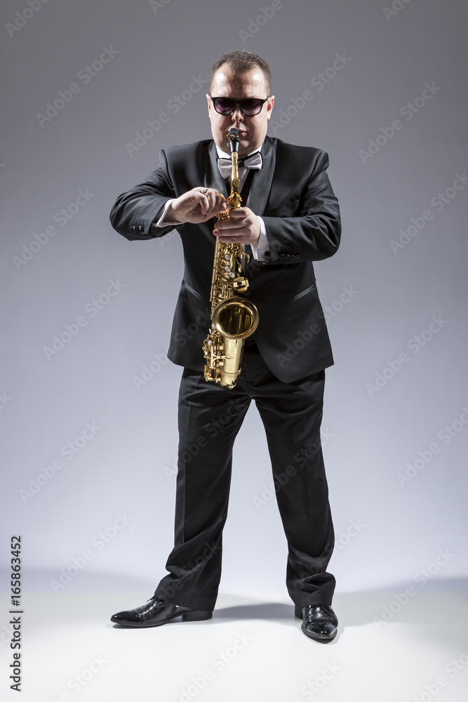 Naklejka premium Music and Musicians Ideas and Concepts. Full Length Portrait of Caucasian Mature Saxophone Player in Sunglasses Playing the Instrument Against White.