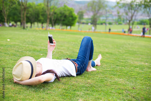 Female student lying on the meadow and using smartphone for texting