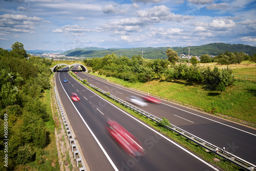 Motion blurred cars on a highway in a landscape with a city in the distance in the background. View from above. © am