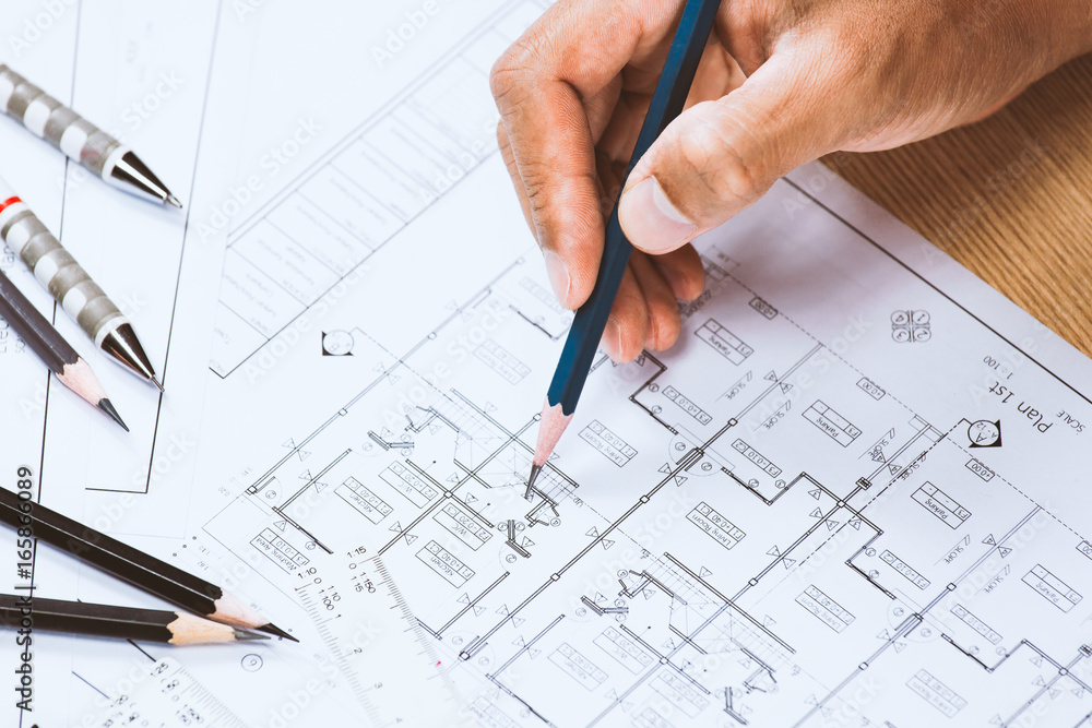 Close-up of person engineer hand drawing plan on blue print with architect instrument at office desk. Close-up of person engineer hand drawing plan on blue print with architect instrument at office desk.