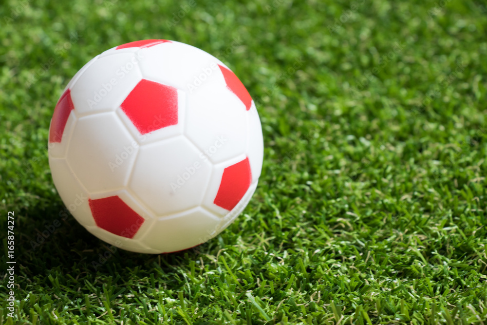 Fototapeta premium Toy red and white color football on artificial green grass background