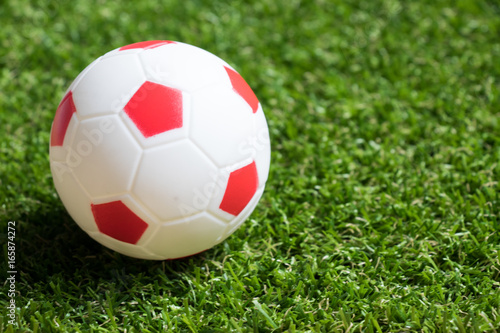 Toy red and white color football on artificial green grass background