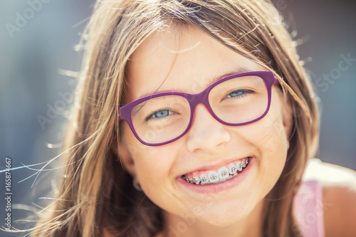 Happy smiling girl with dental braces and glasses. Young cute caucasian blond girl wearing teeth braces and glasses photo