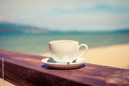 A cup of coffee in a white cup on beach background