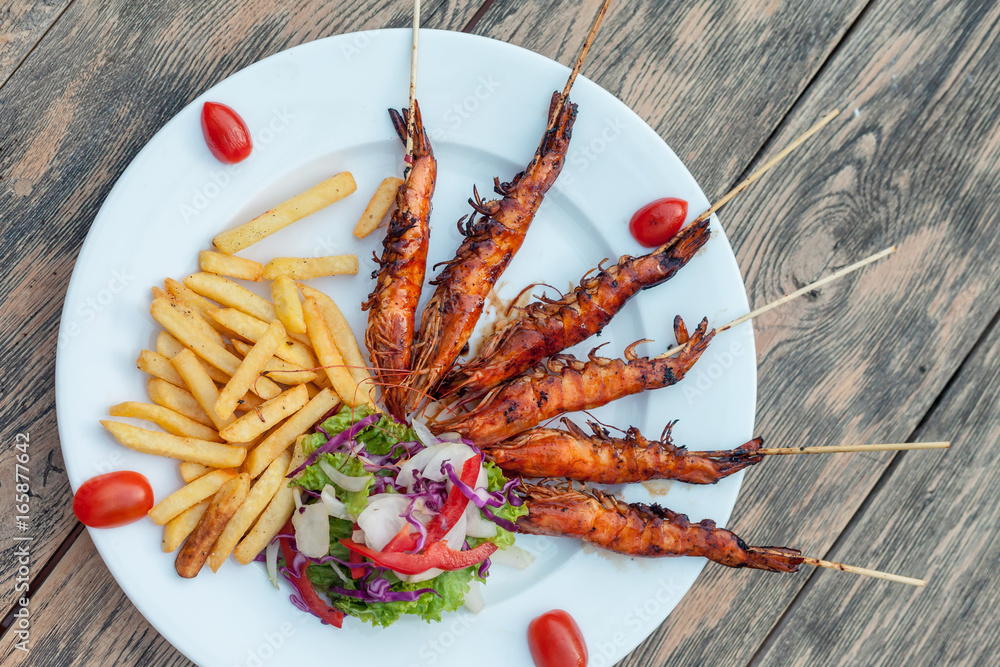 Fried potatoes with fry shrimps, lettuce salad. Isolated over wooden background Fried potatoes with fry shrimps, lettuce salad. Isolated over wooden background