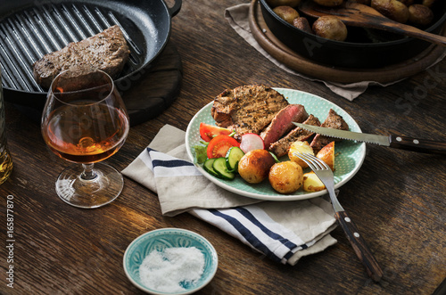 Grilled steak with potatoes, salad and glass of whiskey