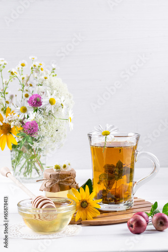 Herbal tea with herbs and flowers in a glass tea pot with honey. Bouquet of flowers on white table