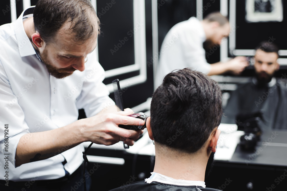 Master cuts hair and beard of men in the barbershop, hairdresser makes hairstyle for a young man Master cuts hair and beard of men in the barbershop, hairdresser makes hairstyle for a young man