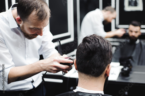 Master cuts hair and beard of men in the barbershop, hairdresser makes hairstyle for a young man