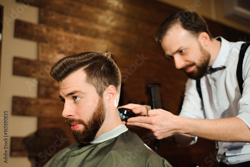 Master cuts hair and beard of men in the barbershop © nagaets