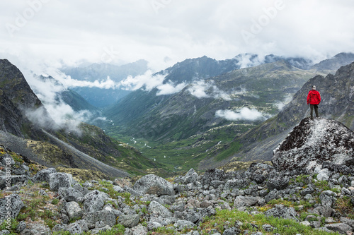 Man in red jacket standing on boulder overlooking glacially carved valley in THe Talkeetna Range, Alaska