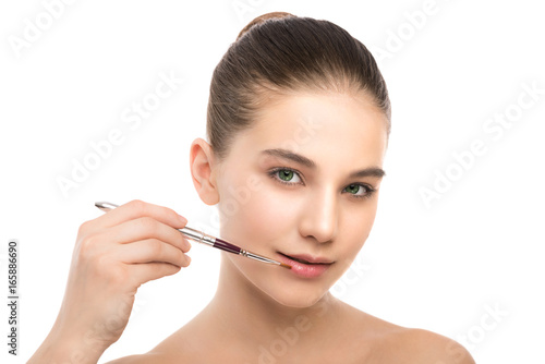 Portrait of beautiful young brunette woman with clean face. Beauty spa model girl with perfect fresh clean skin applying cosmetic brush. Youth and skin care concept. Isolated on a white background.