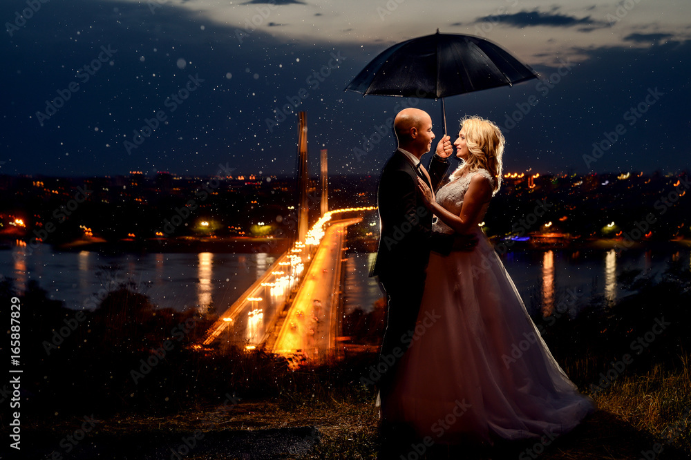 Romantic loving couple newlywed, wedding against background of the night sky. It's raining, the groom and the bride are standing, in love under umbrella. Romantic loving couple newlywed, wedding against background of the night sky. It's raining, the groom and the bride are standing, in love under umbrella.