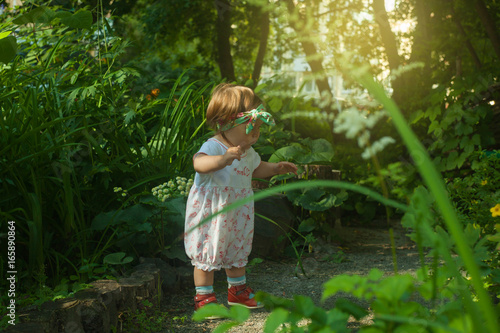 Happy little 1 years girl doing fist steps in summer garden in sunny day, toned photo