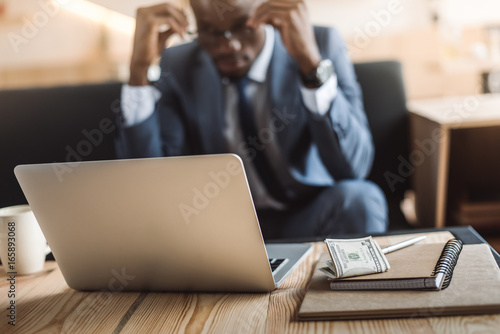 tired african american businessman working with laptop and notepads in cafe