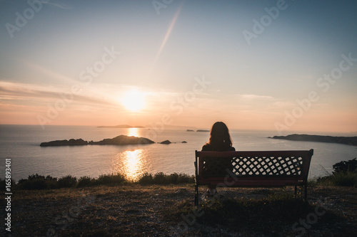 Woman sitting on bench looking at sun